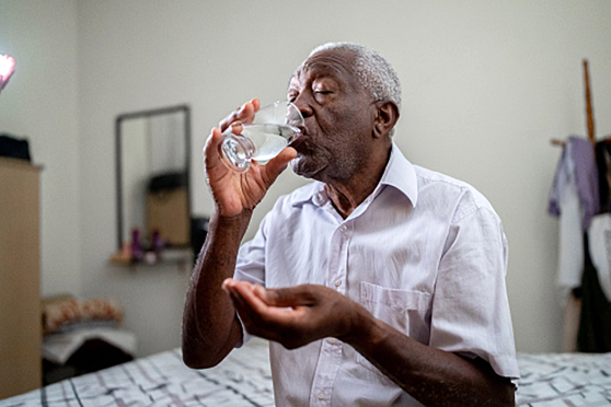 A man holding a pill and drinking from a glass of water
